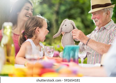 Three generations family gathered to picnic in the garden in summer, focus on a grandfather playing with his granddaughter with her stuffed animal. Shot with flare - Powered by Shutterstock