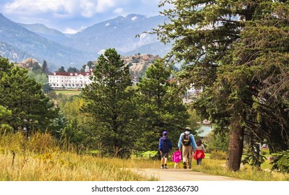 Three Generations Of Family Hiking Near Estes Park, Colorado, In Summer; Building And Mountains In Background