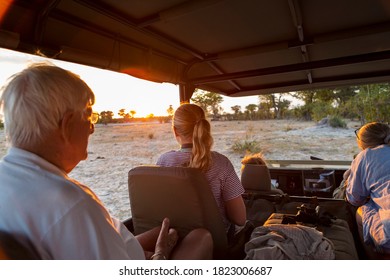 Three Generations Of A Family On Safari, In A Jeep Out At Sunset.