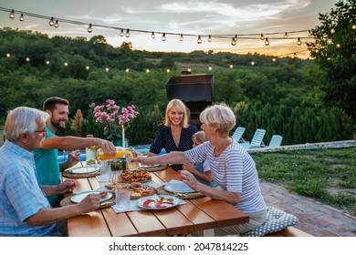 Three generations family sitting at the dining table in the backyard. Little girl enjoying dinner with her parents and grandparents outdoors. - Powered by Shutterstock