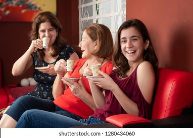 Three Generations Of Hispanic Women Laughing And Drinking Coffee At Home