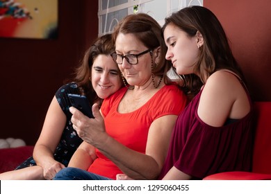 Three Generations Of Hispanic Women Looking At A Smartphone At Home