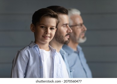 Three Generations. Intergenerational Family Of 3 Diverse Age Men Older Hoary Grandfather Young Handsome Father Little Junior School Age Boy Son Grandson Stand In Row. Focus On Child Looking At Camera