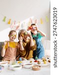 Three generations laughing while preparing for Easter, holding painted eggs over their eyes