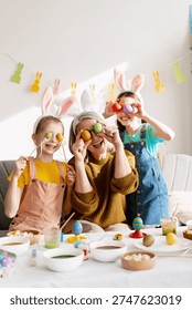Three generations laughing while preparing for Easter, holding painted eggs over their eyes