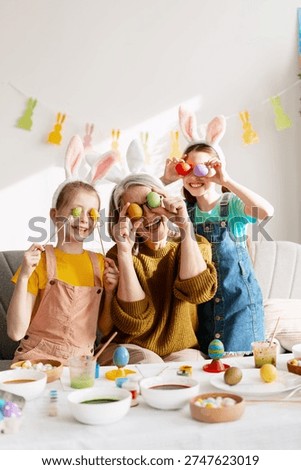 Three generations laughing while preparing for Easter, holding painted eggs over their eyes