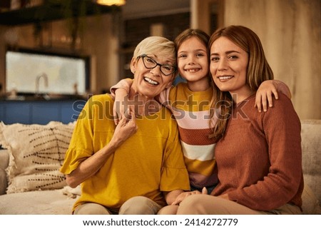 Three generations posing for the camera, sitting on the couch, little girl with her mother and grandma.