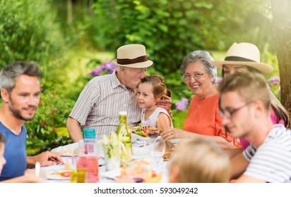 Three generations of the same family having fun while they lunch around a picnic table in summer. Shot with flare