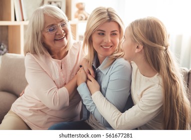 Three generations of women. Beautiful granny, mother and daughter are hugging, talking and smiling while sitting on couch at home