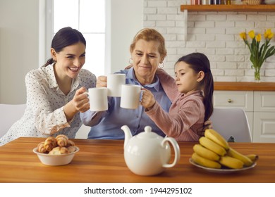 Three generations of women of one family drinking tea together sitting at home in the kitchen. Oder woman with an adult daughter and a little granddaughter are having fun together and clinking cups. - Powered by Shutterstock