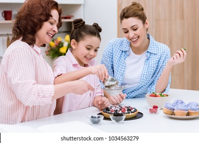 three generations of women pouring sugar onto tart with berries together at kitchen