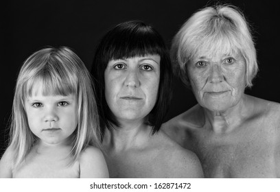 Three Generations Of Women From The Same Family Looking At The Camera In Black And White. Studio Shot On A Black Background.