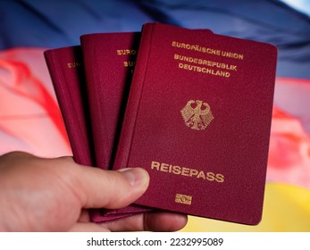 Three German Reisepass (in German: EU, GERMANY, Passport) passports in hand in front of the German flag - Shutterstock ID 2232995089
