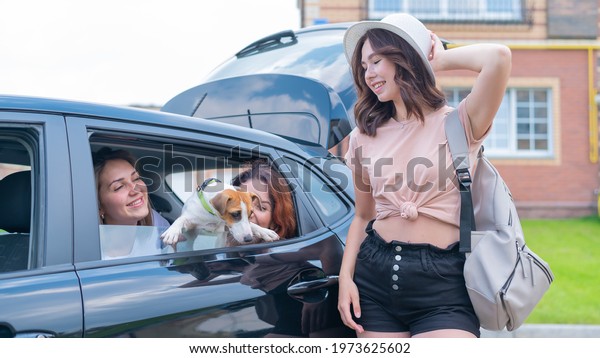 Three girl friends are traveling in a car with a\
dog. Two women are sitting in the back seat with a Jack Russell\
Terrier and looking out of the window, and the third is standing\
nearby and loads
