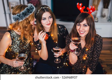 Three Girl At A Home Christmas Party, One Girl Whispering Something To The Other, Looking At The Third Girl.