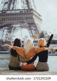 Three girlfriends a brunette, a blonde and a redhead are sitting on the Seine embankment with balloons against the backdrop of the Eiffel Tower. Bachelorette party in Paris.