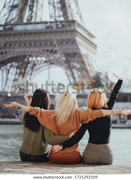 Three girlfriends a\
brunette, a blonde and a redhead are sitting on the Seine\
embankment with balloons against the backdrop of the Eiffel Tower.\
Bachelorette party in\
Paris.