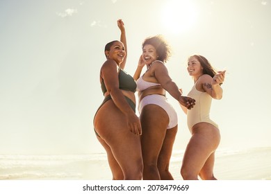 Three girlfriends dancing at the beach. Happy young women smiling cheerfully while dancing in swimwear. Carefree female friends having fun and enjoying their summer vacation.
