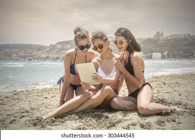 Three Girls At Beach Reading On A Tablet