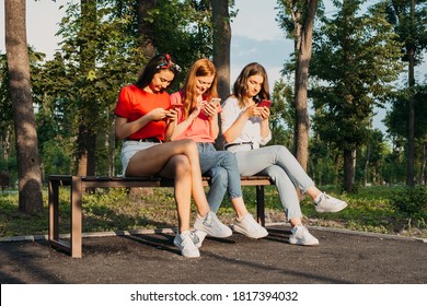 Three Girls Chatting With Their Smartphones At The Park. Gen Z Young Girl Friends Using Gadget And Having Fun Outdoors