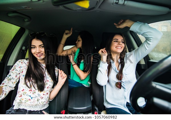 Three girls driving in a car dancing and having\
fun in city street