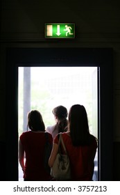 Three Girls Exit The Building On Exit Door. Exit Symbol