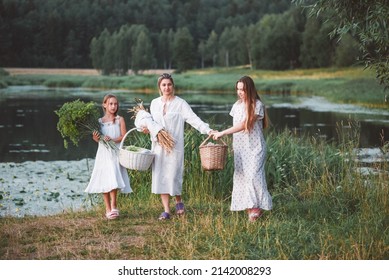 Three girls in long white nightgowns are having fun outdoors by the lake on a warm summer day. Countryside. Three sisters had a picnic by the lake.