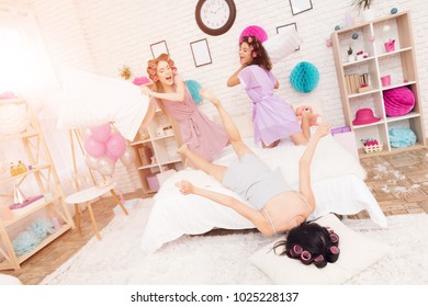 Three Girls In Robes With Curlers In Their Hair Pillow Fight On Bed. They Are Celebrating Women's Day March 8.