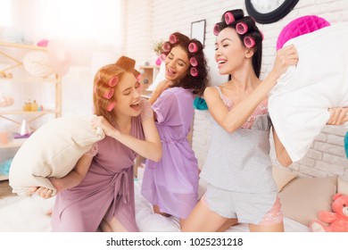 Three Girls In Robes With Curlers In Their Hair Pillow Fight. They Are Celebrating Women's Day March 8.