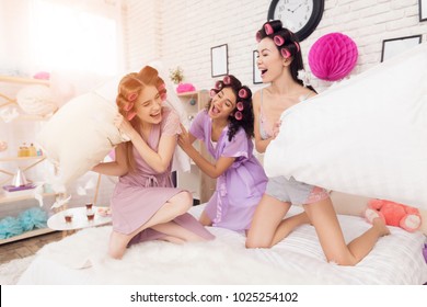 Three Girls In Robes With Curlers In Their Hair Pillow Fight. They Are Celebrating Women's Day March 8.