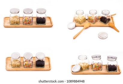 three of glass jar on a rectangular wooden tray containing with raisins, almonds and colorful chocolate. glass jar with four difference angle on white background. isolated