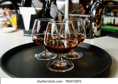 Three glasses with cognac on a dark tray, close-up, service, nightclub.
