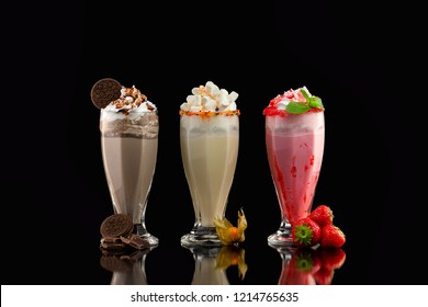 Three glasses of colorful milkshake cocktails - chocolate, strawberry and vanilla decorated with fresh berries and mint isolated at black background.