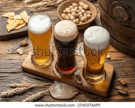 Three glasses of different beer types in beer glass holder and beer snacks on wooden background, top view.
