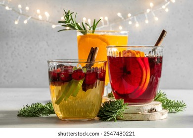 Three glasses of different colored drinks with cinnamon sticks in them. The drinks are cranberry juice, cranberry juice with orange slices, and cranberry juice with orange slices and cranberry juice