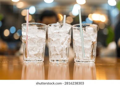 Three glasses of ice and a straw without water are placed on a wooden table at a restaurant