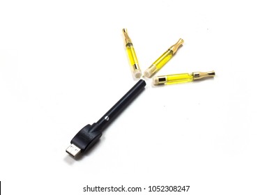 Three Gold Tip Cartridges Of High Grade Cannabis THC CBD Oil And A Black And Silver Weed Vaporizer Smoke Vape Pen With USB Charger Laying Next To Each Other At An Angle