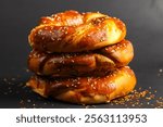 Three golden-brown pretzels stacked atop each other create a tempting display. The soft, shiny surface is accented with sesame seeds and sprinkled seasoning.