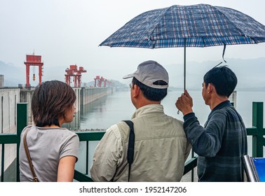 Three Gorges Dam, China - May 6, 2010: Yangtze River. Family Admires Up-river Massive And Long Beige Concrete Dam With Red Flood Control Door Lifts On Top Under Foggy Morning. Umbrella Adds Color.