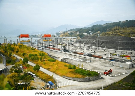 Three Gorges Dam lock system with cargo ship in multi-stage waterway, industrial infrastructure and mountainous landscape backdrop.