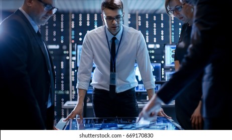 Three Government Agents Working At The Big Table In Monitoring Room. Room Is Full Of State Of The Art Technology. Computers With Animated Screens.