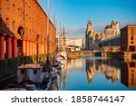 The Three Graces viewed from Royal Albert Dock with historical buildings and reflection in England, United Kingdom.