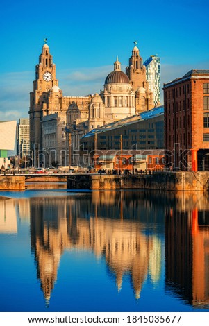 The Three Graces viewed from Royal Albert Dock with historical buildings and reflection in England, United Kingdom.