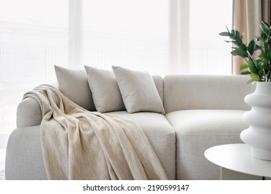 Three grey pillows and blanket on grey soft sofa in living room with panoramic windows. Hypoallergenic concept. Relax idea. Home comfort. House interior details. Hotel room interior design