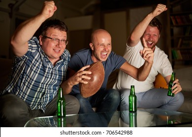 Three Guys Cheering In Front Of TV While Watching American Football Game