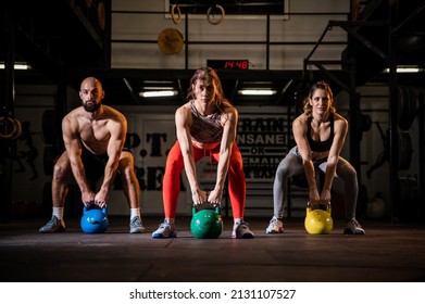 Three gym friends doing a full body workout in the modern enterior gym lifting heavy weights and doing sqauts sweating in their sportswear. Group training. Healthy lifestyle concept.