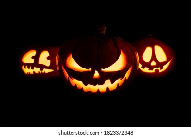 Three Halloween Pumpkins With Glowing Eyes And Mouth On A Black Background	