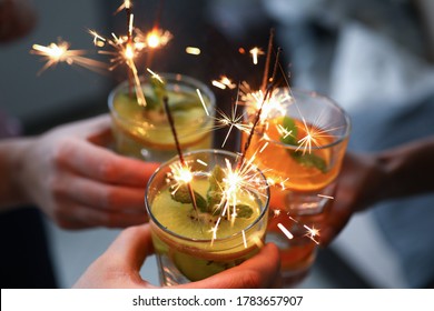 Three hands hold three glasses with cocktail and sparklers close-up. In glass alcohol is poured with pieces of fruit and sparks burn. Friends celebrate birthday and clink glasses. Company celebrates - Powered by Shutterstock