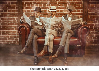 Three handsome men in elegant suits sit on a leather sofa, smoke cigars and read newspapers. Newspaper editorial office. Retro style. Men's fashion.