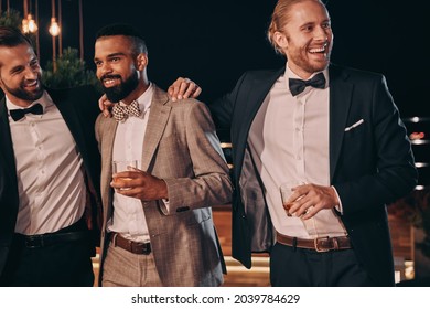 Three handsome men in suits bonding and drinking whiskey while spending time on party